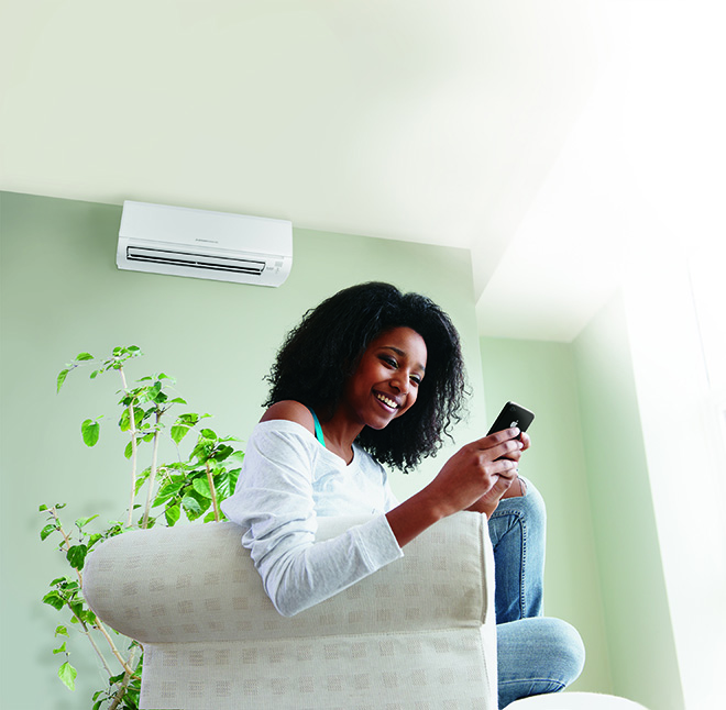 Woman using phone in comfort with Ductless Mini Split Unit on wall